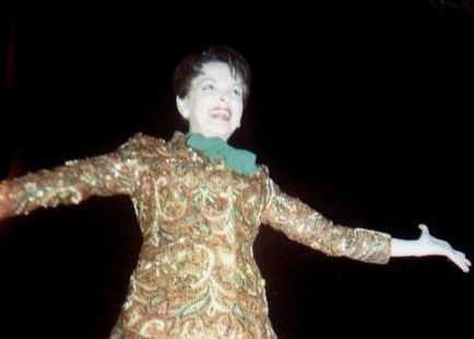 Judy Garland with arms open in gold suit