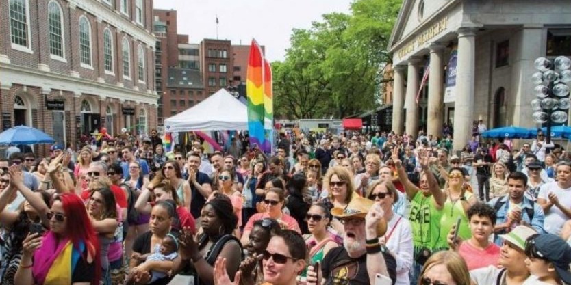 Image from cover of "Hub of the Gay Universe," depicting crowd of people waving and clapping with pride banners at Quincy Market